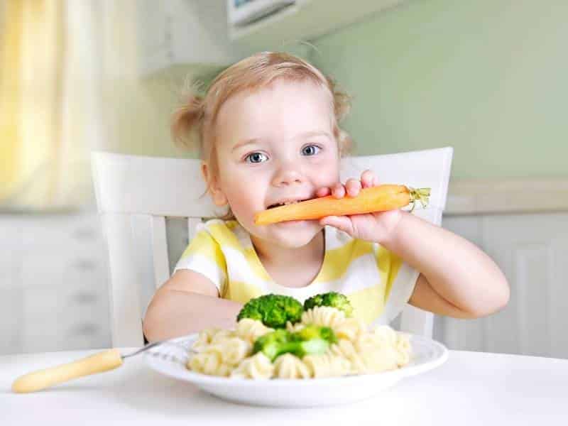 Bambina che mangia carote e cibi salutari